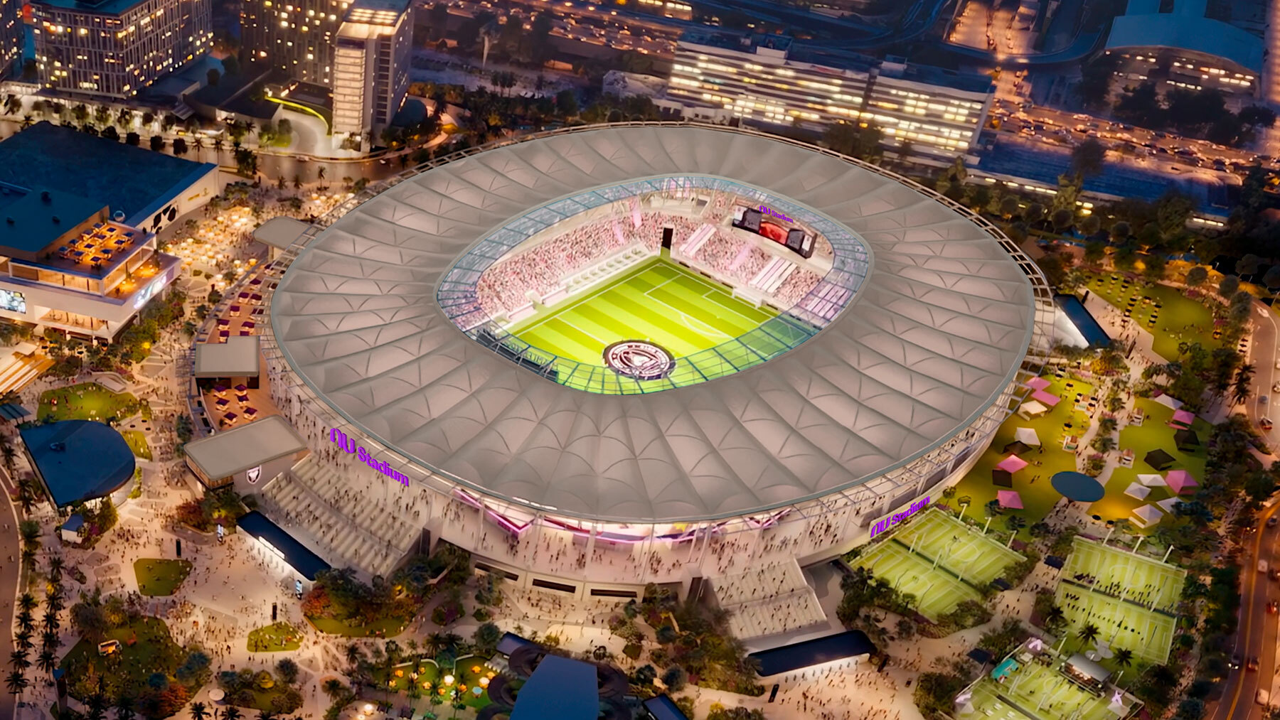 Aerial view of NU Stadium at night with illuminated field, surrounding plaza, and crowds