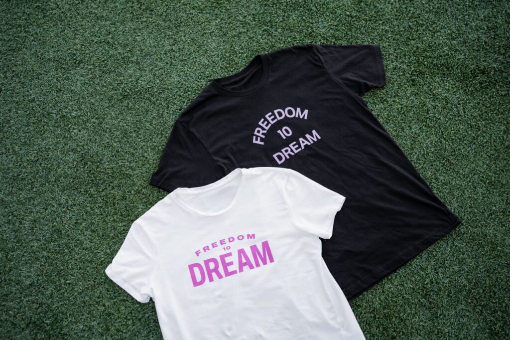 Black and white shirts with “Freedom to Dream” text displayed on grass