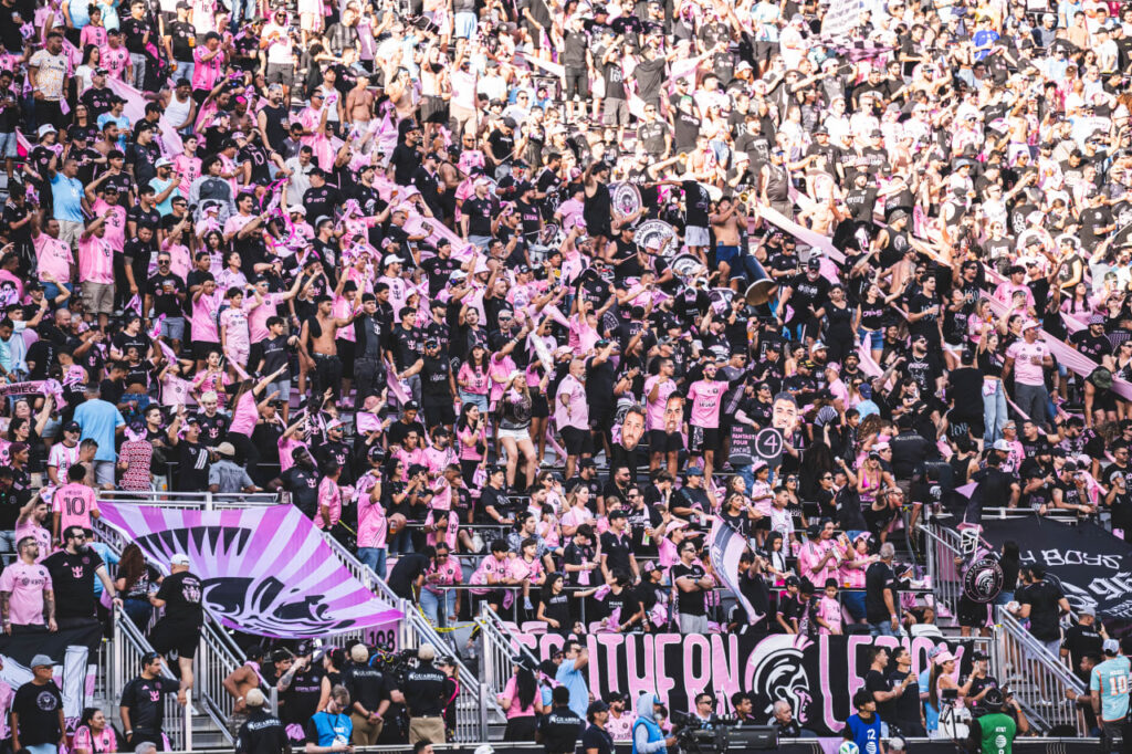 Large crowd of Inter Miami fans wearing pink and black cheering in stadium stands