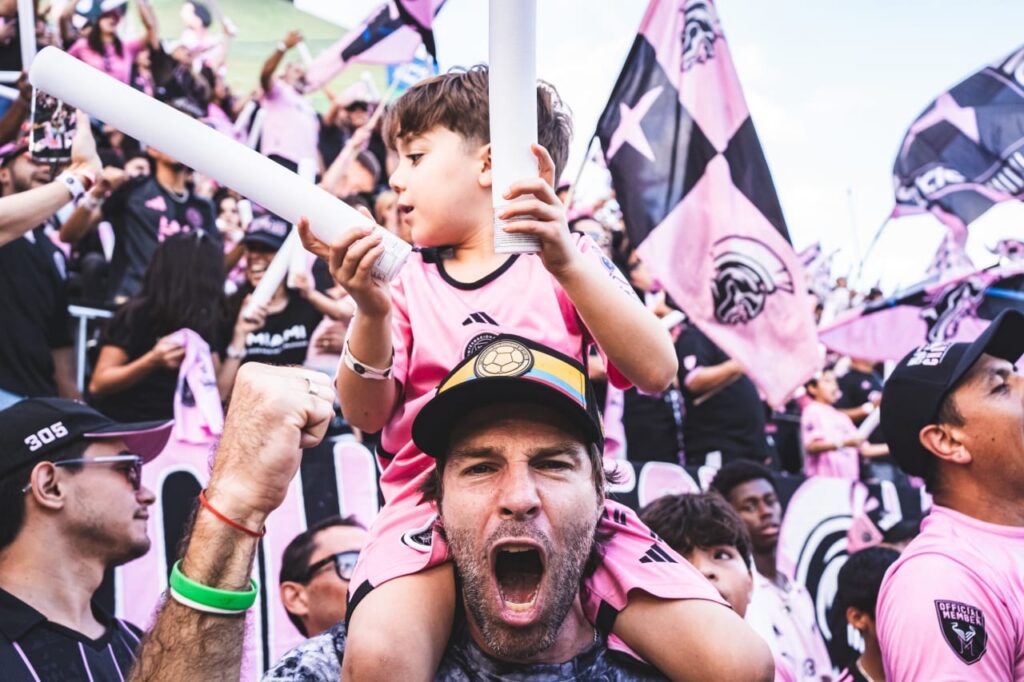 Man with child on shoulders cheering among Inter Miami fans