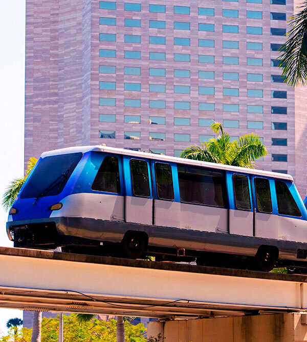 Elevated train traveling on track with city building and palm trees in the background