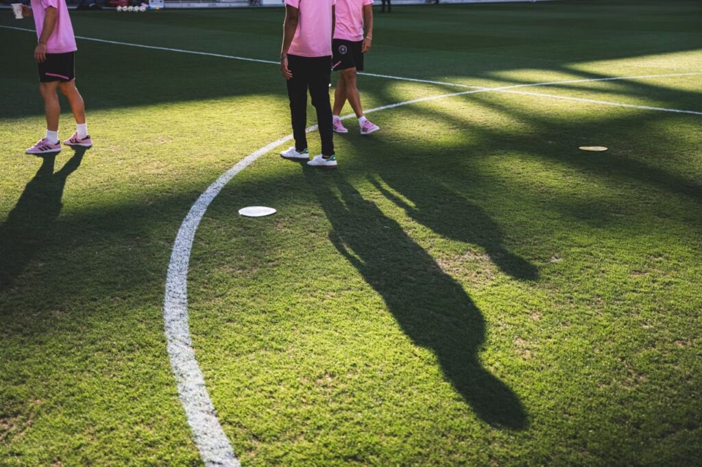 Soccer players standing on field with long shadows cast across green grass