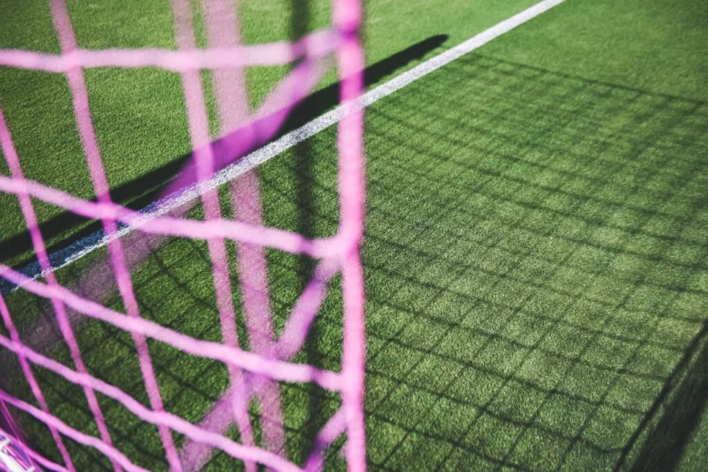 Close-up of pink soccer goal net casting shadows on the field