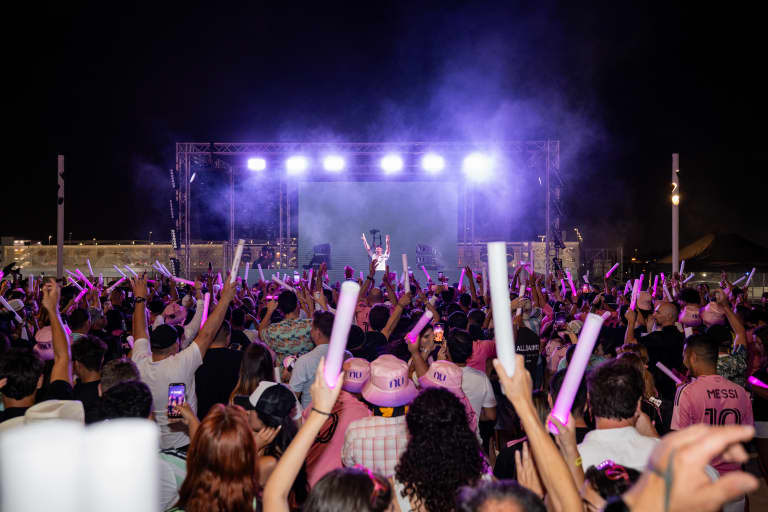 Crowd at nighttime concert waving light sticks under stage lights