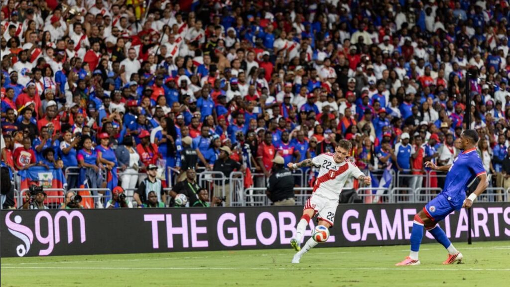 Peru soccer player takes a shot against Haiti during an international match in front of a packed stadium crowd.